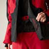 Nahaufnahme einer Person in roter und schwarzer Jacke und roter Hose; Jacke geöffnet, innere Reißverschlussklappe mit kleinen Symbolen, Hände halten die Klappe, heller Hintergrund