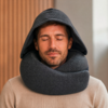 Personne aux yeux fermés, coussin de nuque sombre autour du cou et capuche relevée, pull beige, lambris en bois et mur clair en arrière-plan
