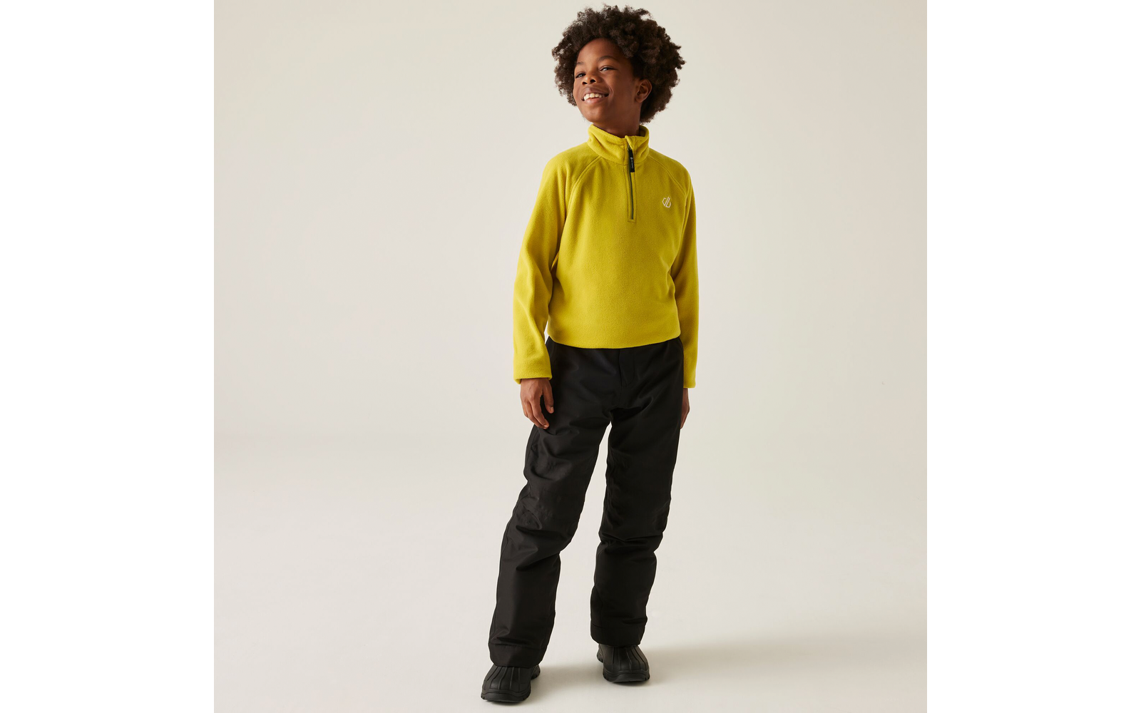 Ein stehendes Kind trägt einen gelben Pullover und schwarze Hosen