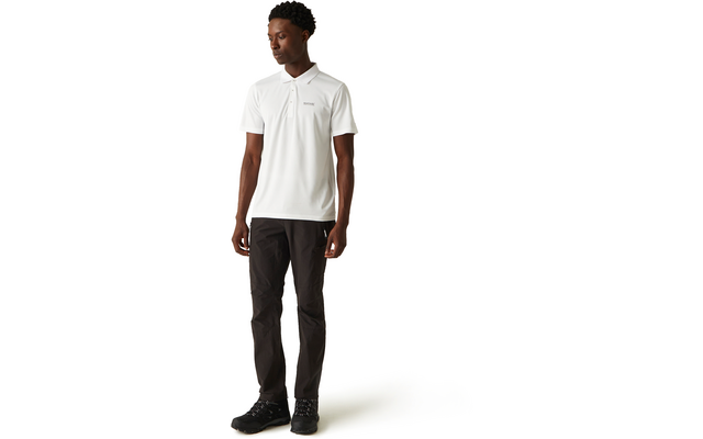 Stehende Person mit dunkler Haut und kurzen lockigen Haaren, trägt weißes Poloshirt mit kleinem Logo links auf der Brust, schwarze Hose und schwarze Schuhe, Blick nach links