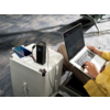 Offener Laptop auf einem weißen Koffer, daneben ein Smartphone, eine Person tippt auf der Tastatur