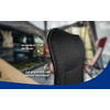 Black chair backrest with 3D-mesh fabric, white German labels "besonderer Stoff: 3D-Mesh" and "gut gepolstert und schnell trocknend" with arrows, blurred interior background and blue curved area at the bottom