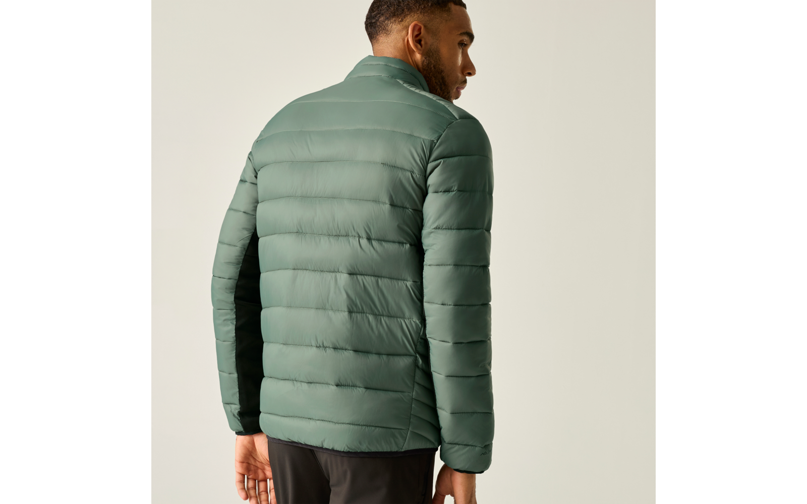 Mann von hinten, trägt hellgrüne gesteppte Jacke und dunkle Hose, schaut nach rechts, einfarbiger heller Hintergrund