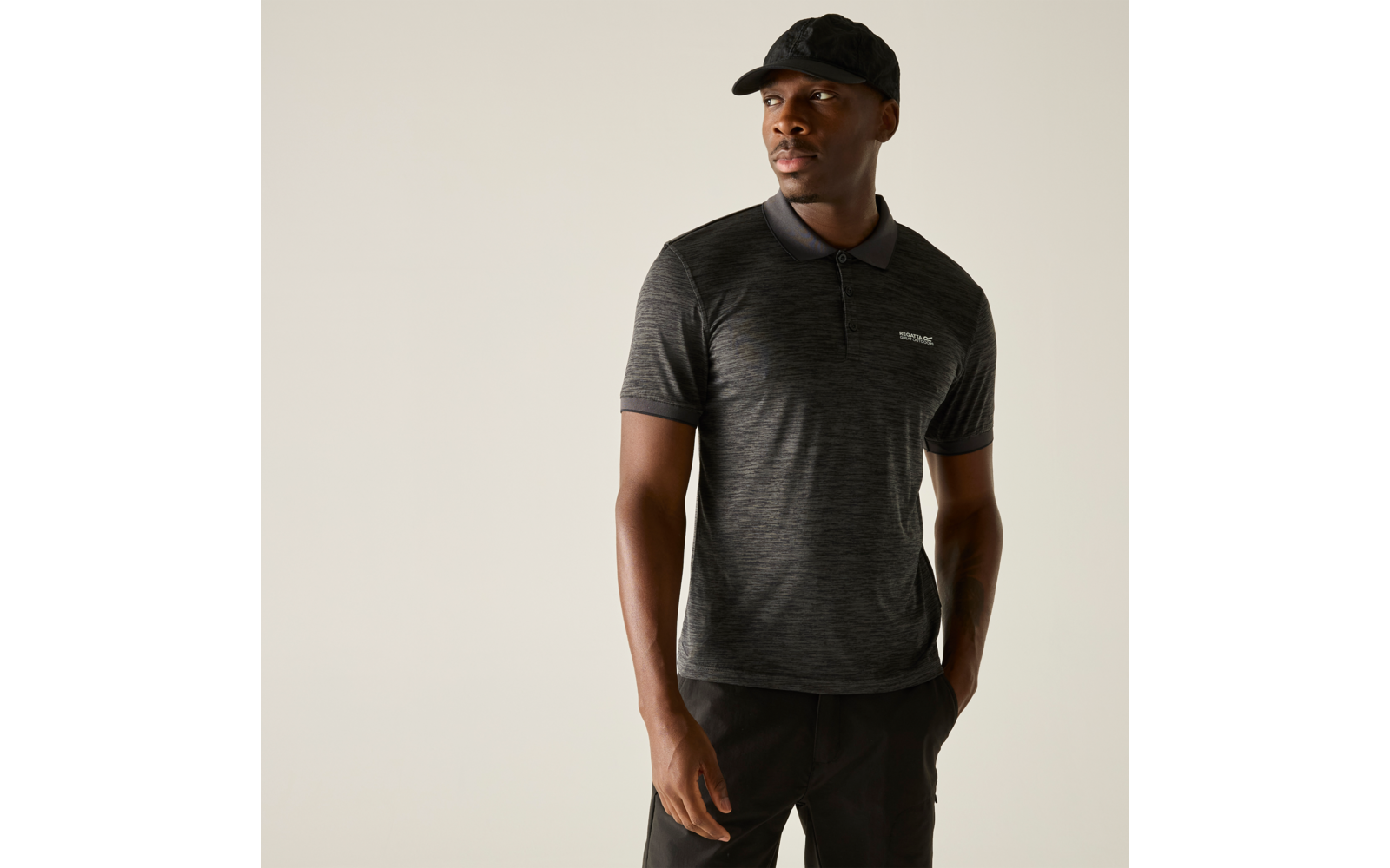Persoon met donkergrijs kort mouw polohemd met klein borstlogo en zwarte pet, staand voor een effen lichte achtergrond en kijkt opzij