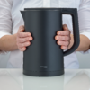 Persona che tiene un bollitore elettrico nero con entrambe le mani su uno sfondo bianco