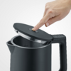 Mano che tocca il coperchio aperto di un bollitore nero