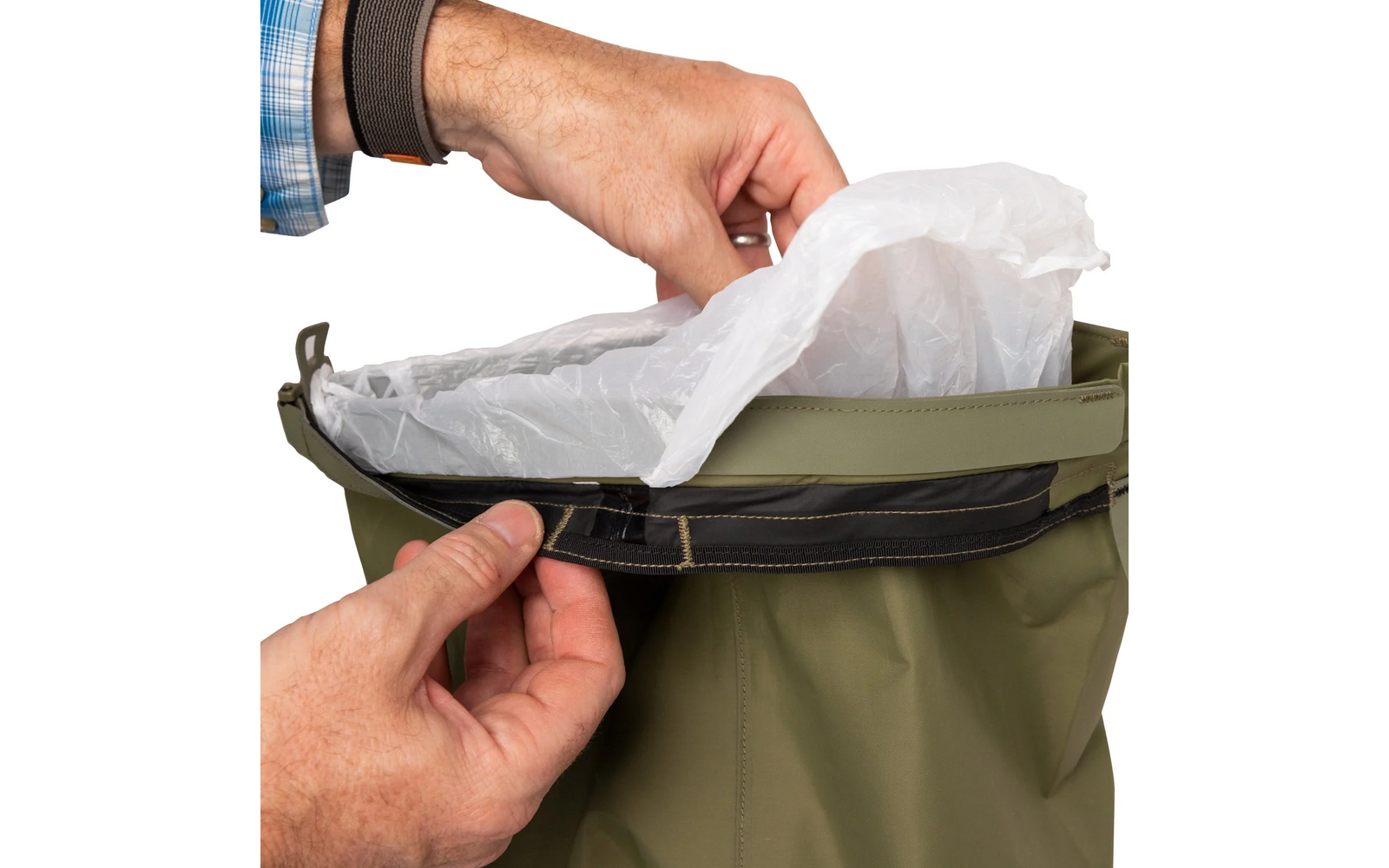 Deux mains : l'une tient le bord supérieur d'un vêtement imperméable olive à finition noire, l'autre introduit un sachet plastique blanc translucide