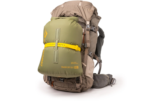 Grand sac à dos beige avec un drybag olive fixé à l'avant, sangle jaune, inscription "TRASH DRY BAG 10L", ceinture de hanche et boucles visibles