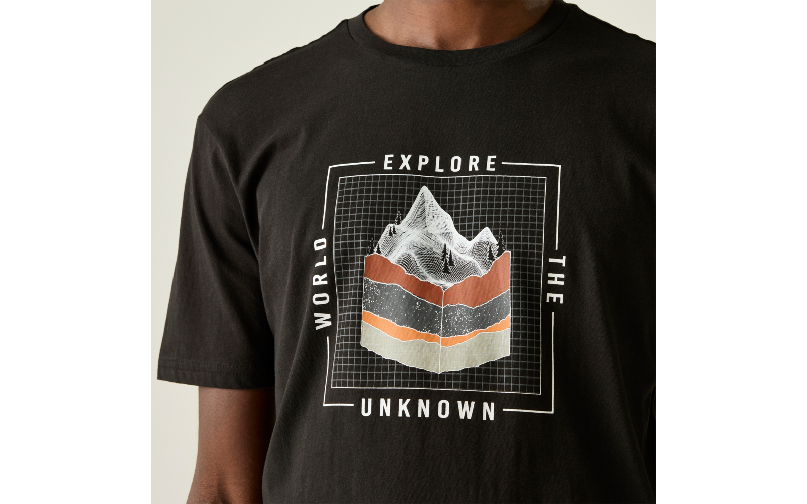 Oberkörper einer Person in schwarzem T‑Shirt mit quadratischer Grafik: Rasterhintergrund, weiße Bergsilhouette, drei horizontale Schichten in Orange, Dunkelgrau und Beige; Text 'EXPLORE' oben, 'WORLD' links, 'THE' rechts, 'UNKNOWN' unten