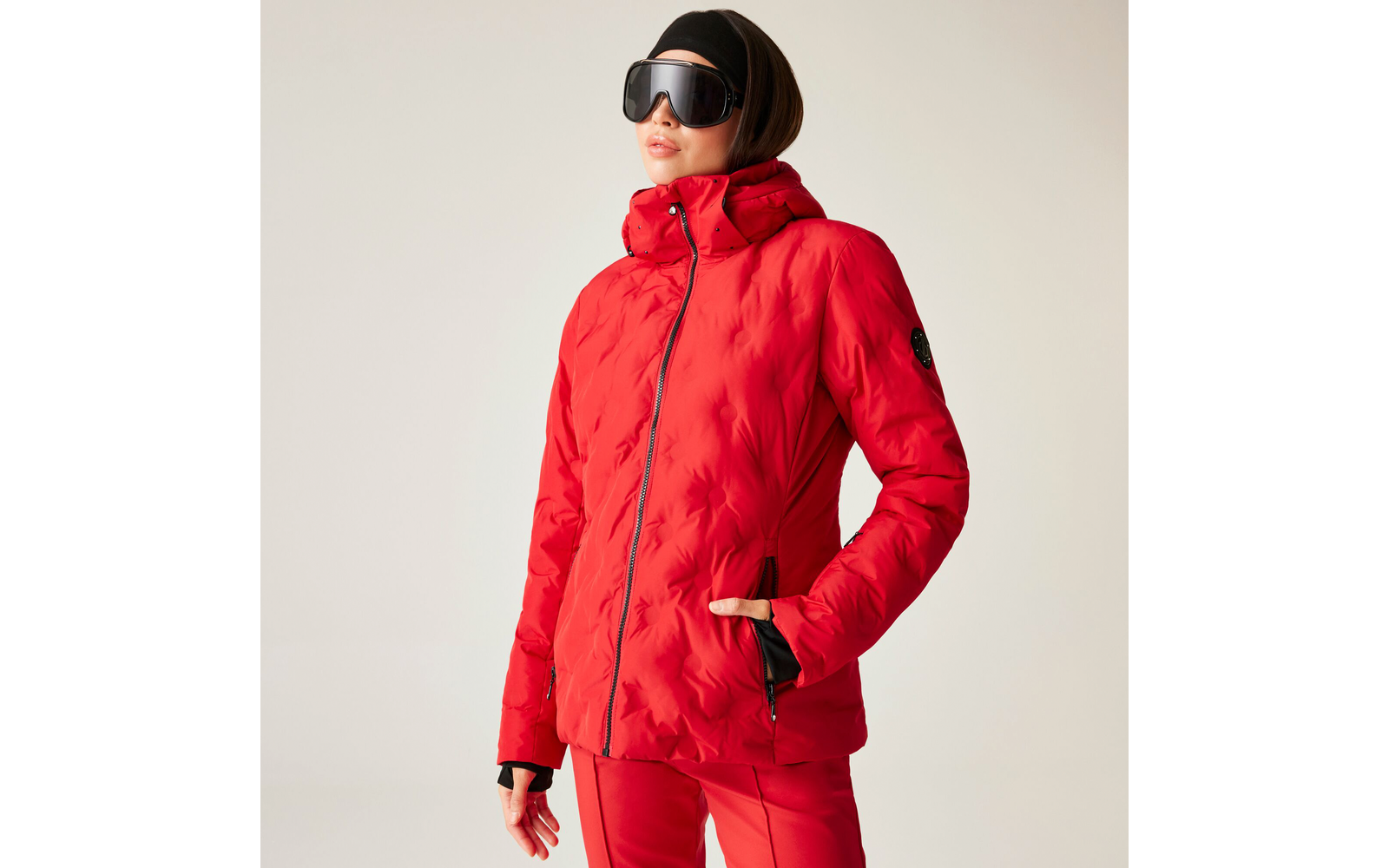 Frau trägt rote Winterjacke und Skibrille vor hellem Hintergrund
