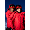 Ein Mann und eine Frau tragen rote Skianzüge und Helme mit Skibrillen vor einem dunklen Hintergrund
