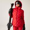 Frau in roter Skijacke und schwarzer Skibrille hält Skier und Stöcke