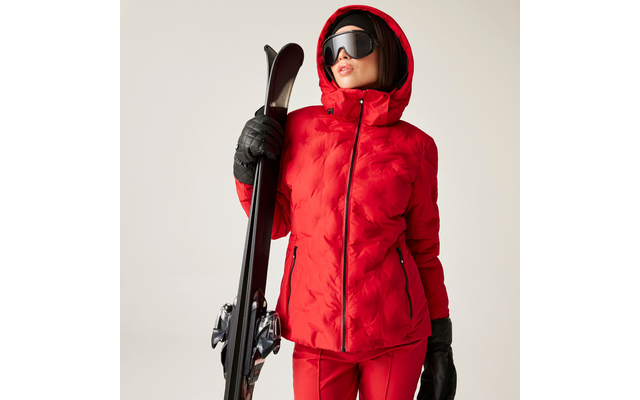 Frau in roter Skijacke und schwarzer Skibrille hält Skier und Stöcke