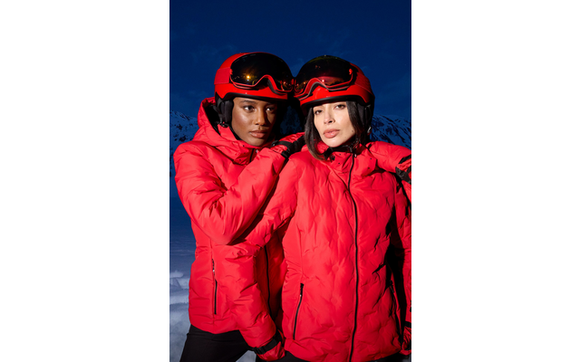 Ein Mann und eine Frau tragen rote Skianzüge und Helme mit Skibrillen vor einem dunklen Hintergrund