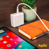 Ladekabel, das an einem weißen Ladegerät angeschlossen ist, liegt auf einem Holztisch neben einem orangefarbenen Notizbuch, einem Smartphone und einem Blumentopf mit einer grünen Pflanze