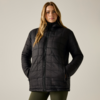 Persona con lunghi capelli biondi, in piedi frontalmente, indossa una giacca imbottita nera trapuntata con cerniera e cappuccio, mani nelle tasche, leggings verde oliva su sfondo chiaro uniforme