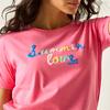 Nahaufnahme einer Person mit rosa T‑Shirt, auf der bunte Stickerei 'Summer love' auf der Brust zu sehen ist; Hals, Kinn und dunkles, welliges Haar sichtbar