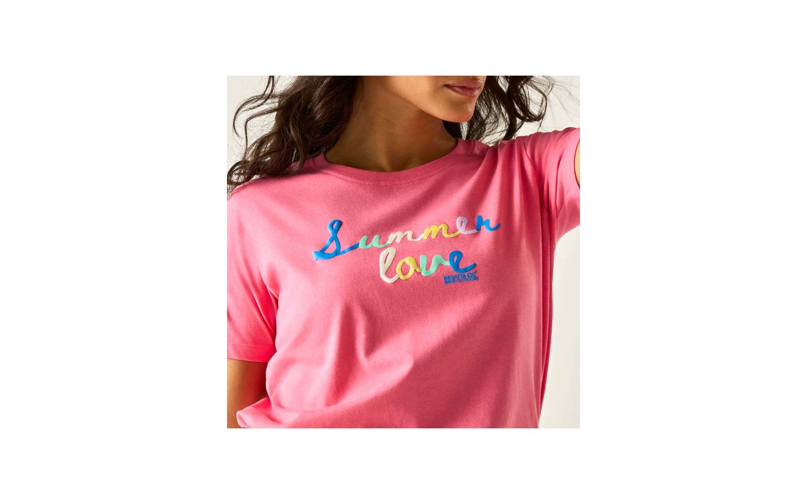 Nahaufnahme einer Person mit rosa T‑Shirt, auf der bunte Stickerei 'Summer love' auf der Brust zu sehen ist; Hals, Kinn und dunkles, welliges Haar sichtbar