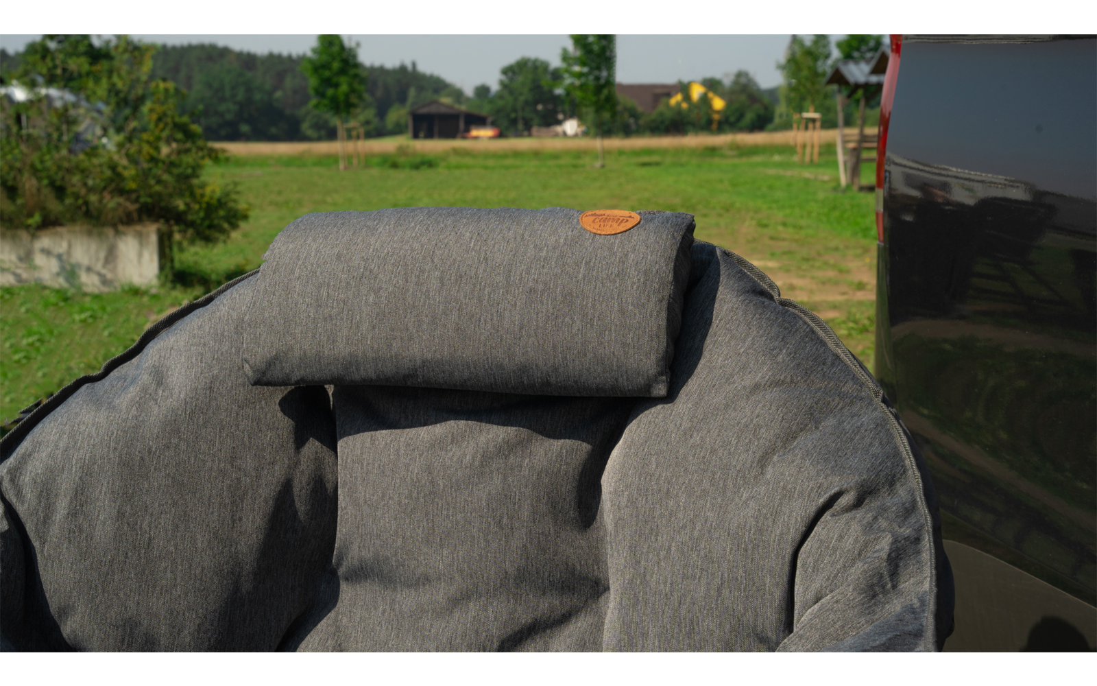 Grauer gepolsterter Sitz mit Kopfstütze im Freien vor einer grünen Wiese und Bäumen