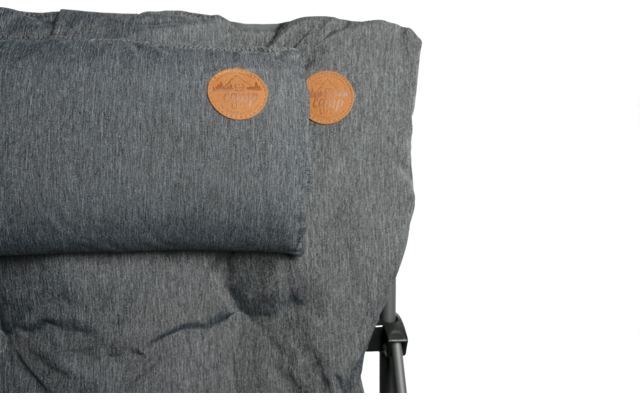 Grau gepolstertes Sitz-/Rückenpolster mit kleinem Nackenrollen-Kissen, zwei runden braunen Lederetiketten oben rechts, sichtbarem Metallrahmen rechts und dunklen Flecken im Stoff