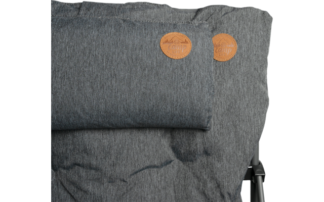 Gray padded seat/back cushion with small neck-roll pillow attached, two round brown leather tags at top right, visible metal frame at right and darker stains on the fabric
