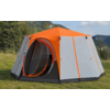 Orange and gray tent with a round open entrance on a grassy meadow; trees, mountains and blue sky in the background