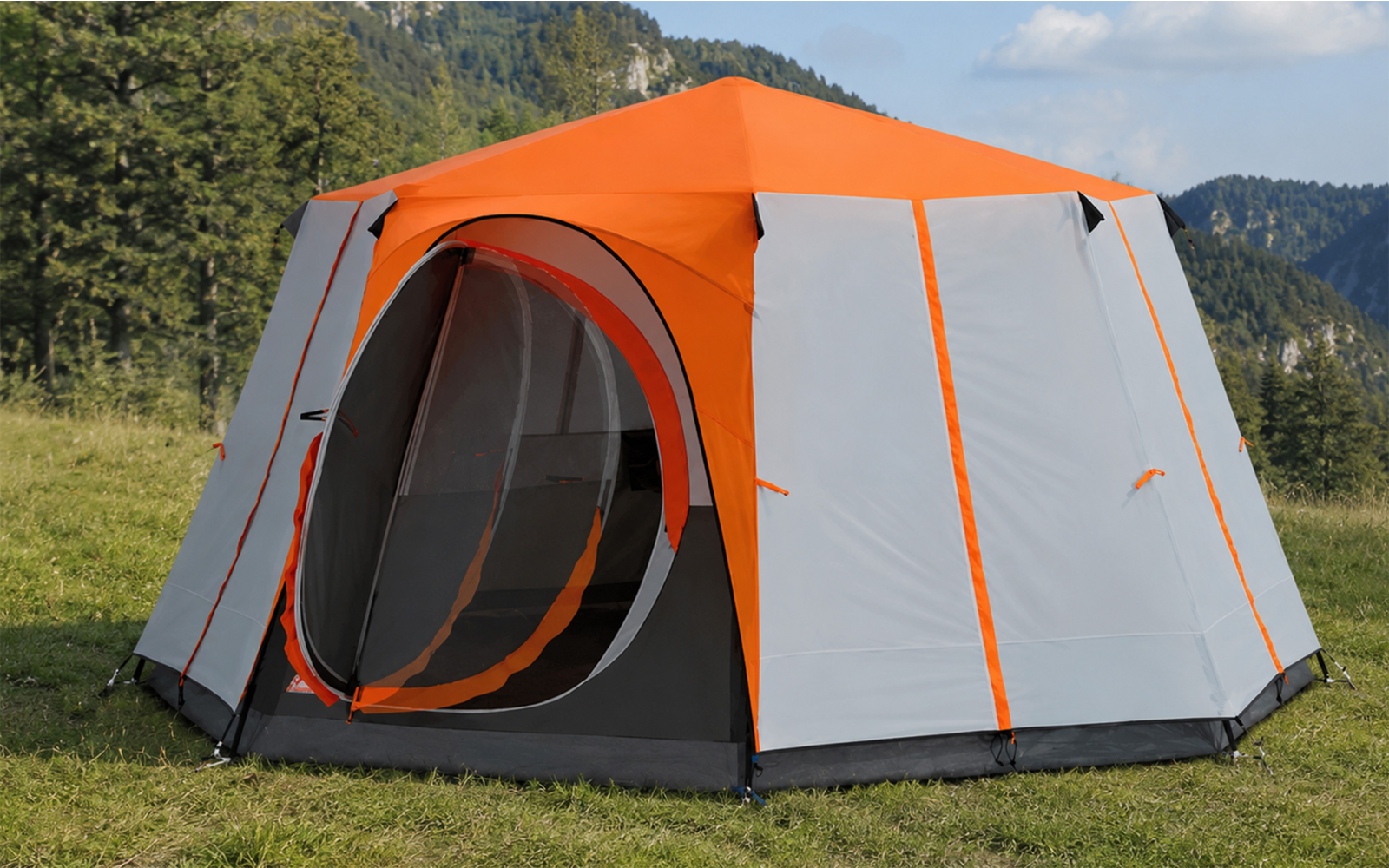 Orange and gray tent with a round open entrance on a grassy meadow; trees, mountains and blue sky in the background