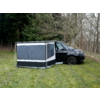Schwarzer Campingbus auf Gras neben kahlen Bäumen, an der Seite ein grau-schwarzes Vorzelt mit geschlossenen Fenstern und weißen Streifen