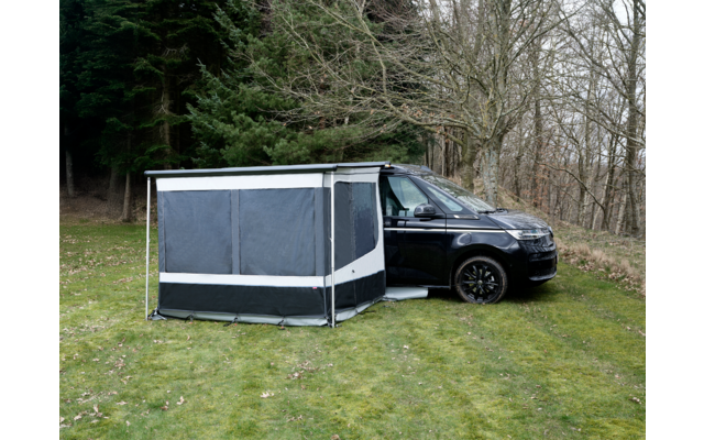 Schwarzer Campingbus auf Gras neben kahlen Bäumen, an der Seite ein grau-schwarzes Vorzelt mit geschlossenen Fenstern und weißen Streifen