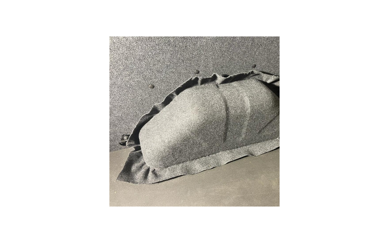 Gewelfde vorm onder zwart, grof getextureerd stof op een donkere ondergrond; stof met plooien en een zichtbare rand, twee kleine ronde openingen in het oppervlak erboven