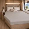 Bed in interieur met houtbekleding, drie kussens, gestoffeerd hoofdeinde, nachtkastje met vaas, raam met uitzicht op meer en bergen