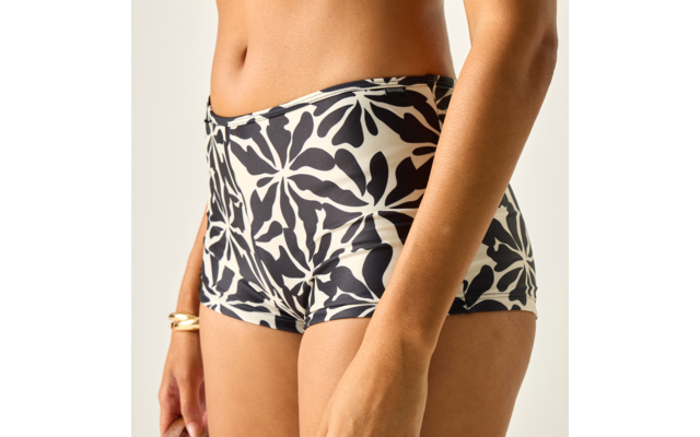 Bauch, Hüften und Oberschenkel in schwarz-weiß geblümten Shorts; rechte Hand mit goldfarbenem Armreif; heller Hintergrund