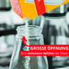 De la poudre est versée d'un carton jaune dans un bocal en verre ouvert ; une flèche rouge et une bande rouge avec le texte blanc 'GROSSE ÖFFNUNG Zum mühelosen Befüllen der Gläser'
