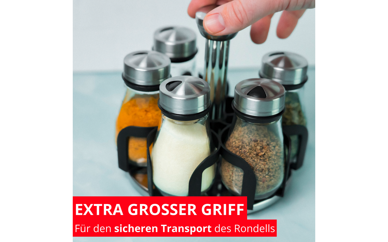 Main saisit un bocal en verre rond avec couvercle métallique dans un support noir; cinq bocaux en verre contenant des poudres colorées (jaune, blanc, brun, vert) sur fond bleu clair; bandeau rouge en bas avec texte blanc 'EXTRA GROSSER GRIFF Für den sicheren Transport des Rondells'
