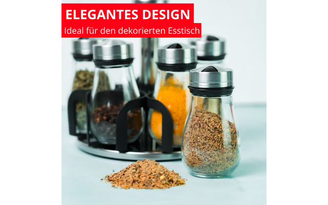 Plusieurs flacons d'épices en verre dans un support rond ; au premier plan un flacon avec une épice brune et un petit tas devant ; à l'arrière d'autres flacons avec des épices jaunes et vertes ; bannière rouge en haut à gauche avec le texte blanc "ELEGANTES DESIGN Ideal für den dekorierten Esstisch"
