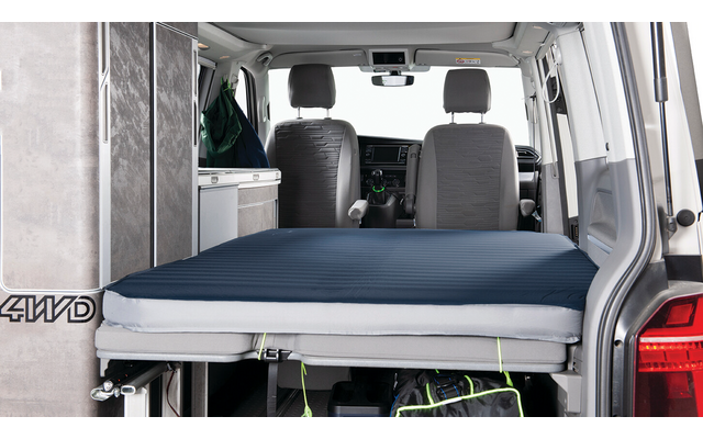 Interior of a van with extended bed: dark blue mattress on a platform, two front seats, cabinet on the left, bag under the platform, open rear door