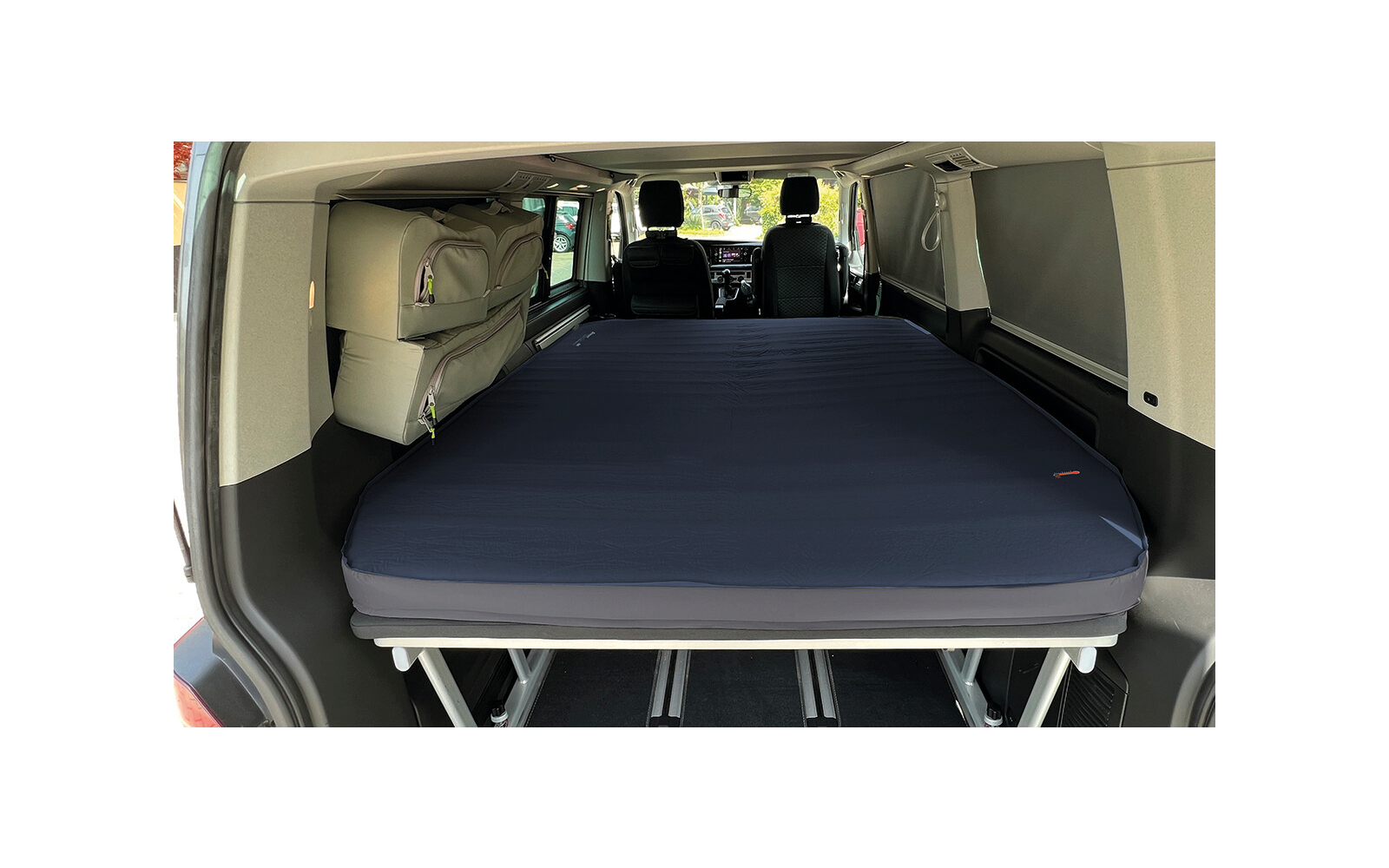 Vehicle interior with a dark blue mattress on a metal frame, two front seats and windows visible