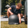 Bearded man in black t-shirt kneeling on grass setting up a black dome near a vehicle