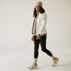 Frau in weißer Jacke, schwarzer Hose, beige Mütze und hellen Schuhen vor weißem Hintergrund