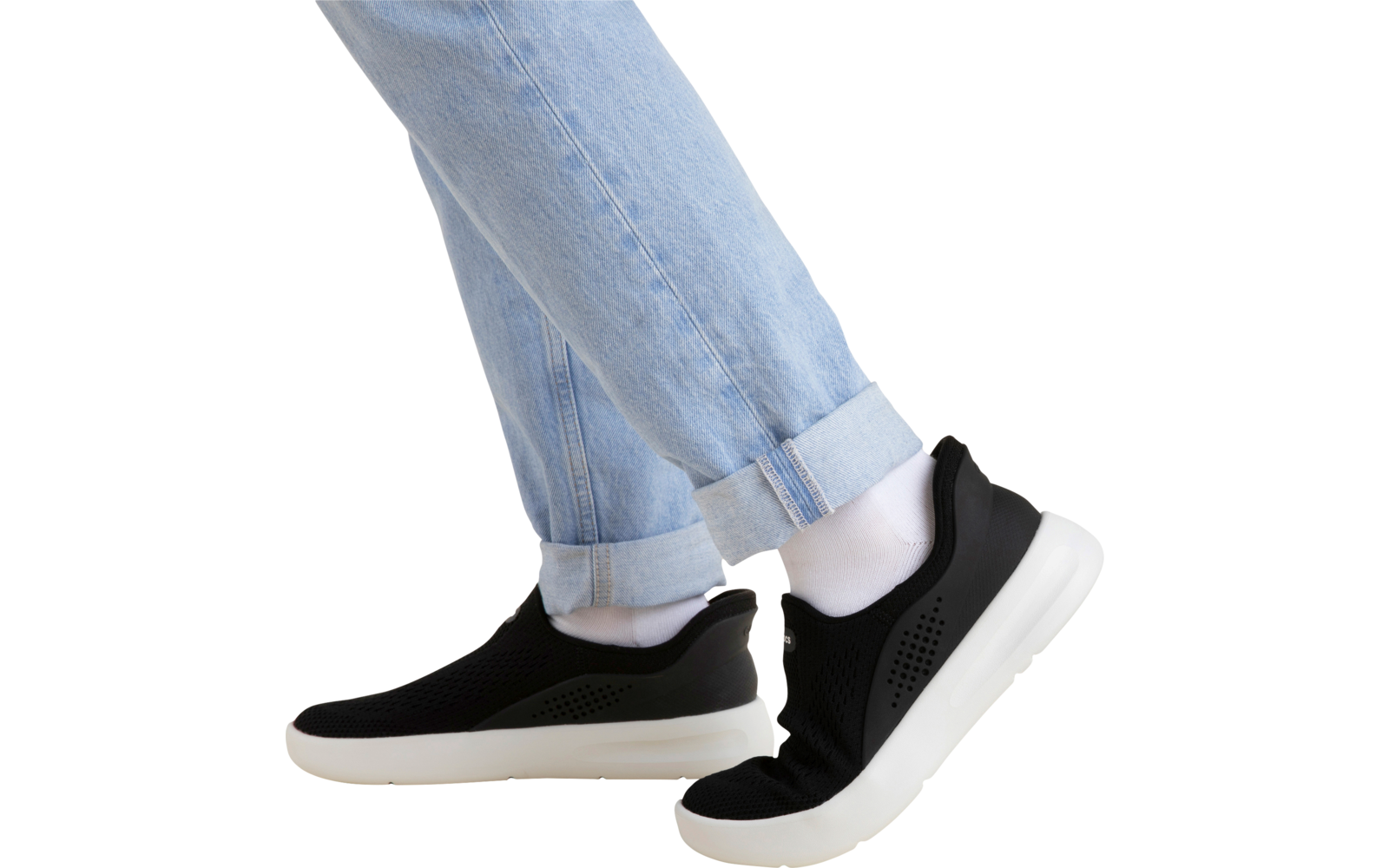 Beinpartie in hellblauen hochgekrempelten Jeans, weiße Socken und schwarze Slip‑on‑Sneaker mit weißer Sohle auf beigem Hintergrund