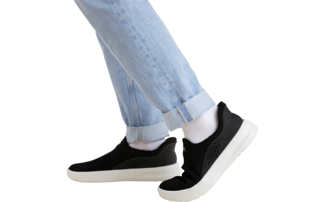 Beinpartie in hellblauen hochgekrempelten Jeans, weiße Socken und schwarze Slip‑on‑Sneaker mit weißer Sohle auf beigem Hintergrund