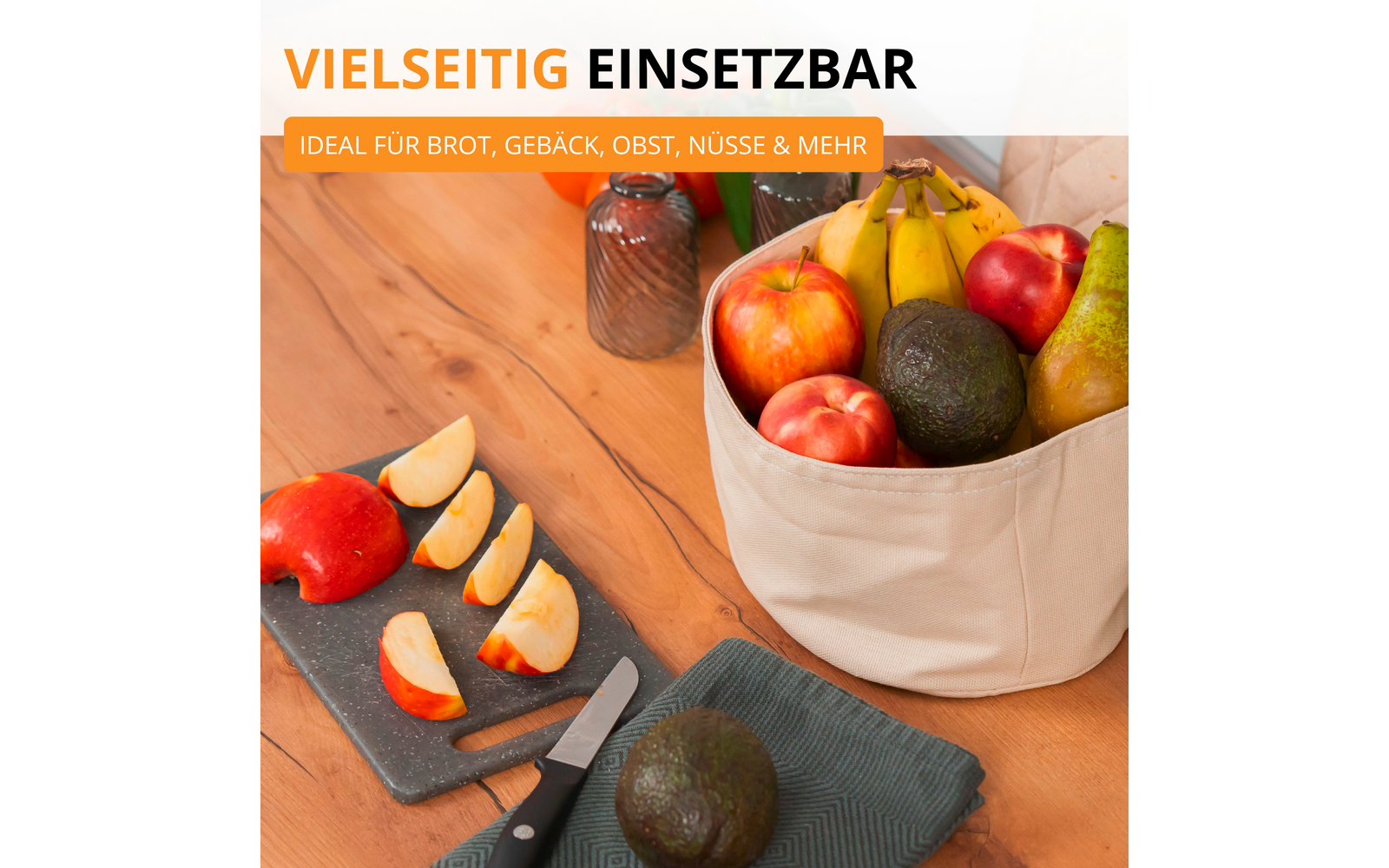 Panier en tissu beige contenant bananes, pommes, avocat, poire et nectarine sur une table en bois; à côté, quartiers de pomme sur une planche foncée, un couteau, un avocat sur un tissu et deux bocaux en verre en arrière‑plan