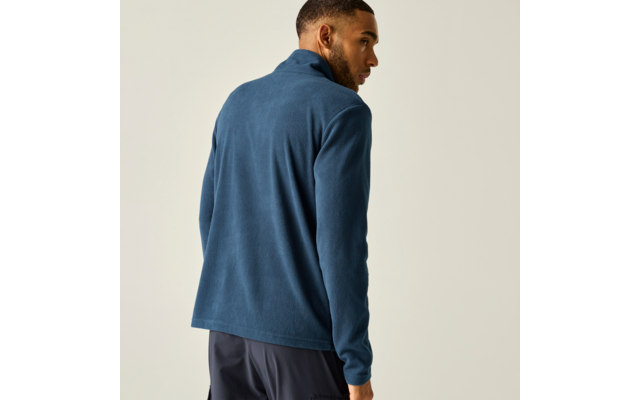 Person von hinten in blauer Fleecejacke und dunkler Hose, schaut über die rechte Schulter, heller Hintergrund
