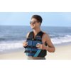 Person mit Schwimmweste und Sonnenbrille steht auf einem Sandstrand und hält die Westenriemen; Meer und Himmel im Hintergrund