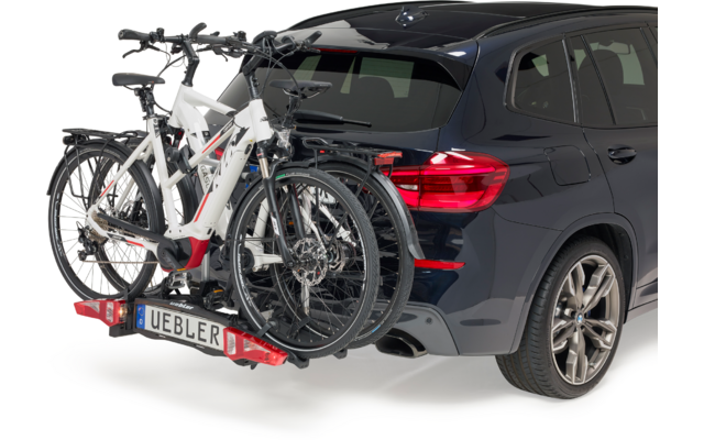 Donkerblauwe SUV van achterrechts met twee witte fietsen op een aan de trekhaak gemonteerde fietsendrager
