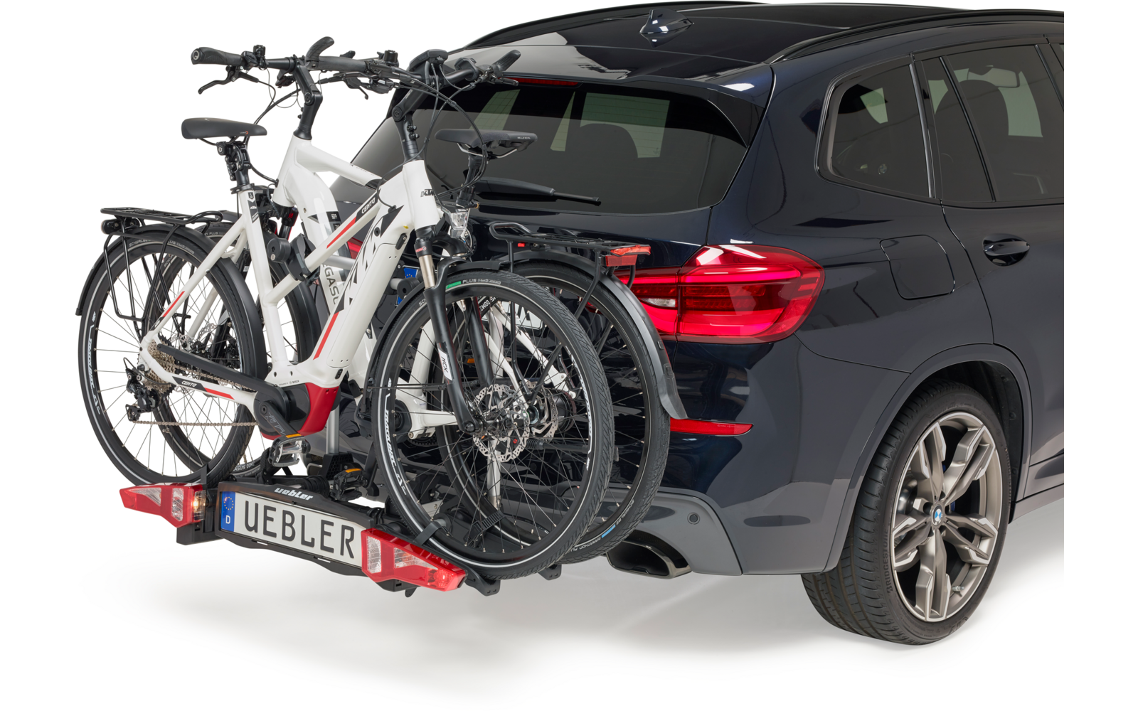 Donkerblauwe SUV van achterrechts met twee witte fietsen op een aan de trekhaak gemonteerde fietsendrager