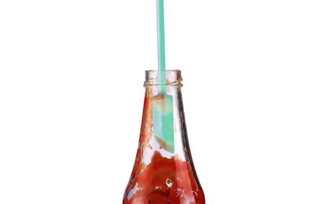 Bouteille en verre avec une sauce rouge épaisse et une spatule turquoise dans l'ouverture ; sauce sur les parois intérieures et le rebord