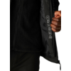 Eine Person trägt eine schwarze Jacke, die geöffnet ist, und hält sie mit der rechten Hand