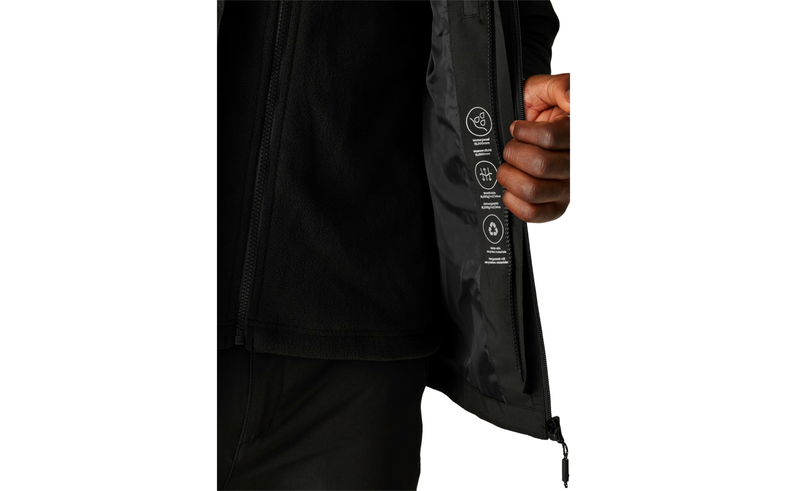 Eine Person trägt eine schwarze Jacke, die geöffnet ist, und hält sie mit der rechten Hand