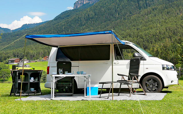 Wohnmobil mit ausgefahrener Markise, Campingstühle und Klapptisch im Grünen